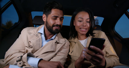 Diverse couple riding in cab and surfing internet on smartphoneの写真素材