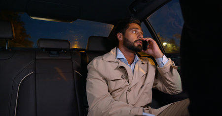 Young confident man talking over phone while sitting in taxiの写真素材