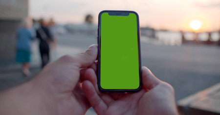 Pov bokeh shot of man hands holding modern black mobile phone with blank green screen.の写真素材