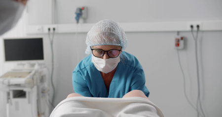 Obstetrician in safety cap and mask assisting woman in laborの写真素材