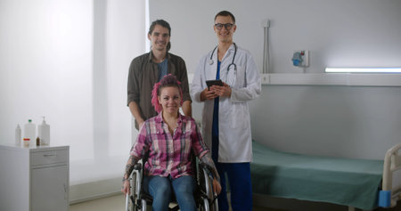 Portrait of woman patient in wheelchair, husband and doctor smiling at camera in hospital wardの写真素材