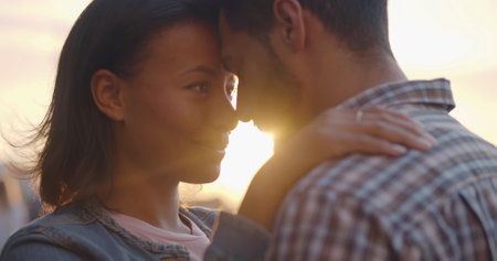 Closeup of multiracial young couple in love hug and touch foreheads on street in eveningの写真素材