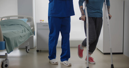 Doctor helping female patient in crutches at hospital wardの写真素材
