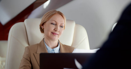 Close up of mature businesswoman reading contract and discussing with partner flying in first classの写真素材