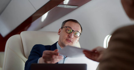Successful businessman and businesswoman reading and discussing documents flying on private jetの写真素材