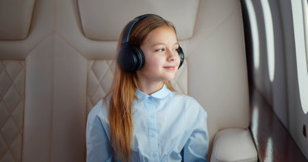 Preteen girl in headphones sitting in airplane looking through windowの写真素材