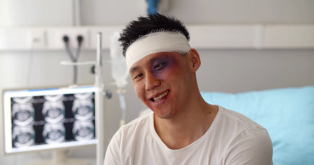 Male patient with bandaged head and bruised face acting crazy in hospital wardの写真素材