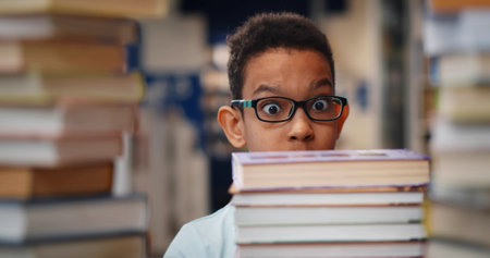 Close up of African-American kid feeling shocked looking at large stack of book on tableの写真素材