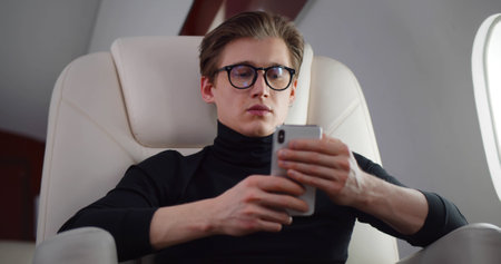 Young handsome man using smartphone flying business classの写真素材