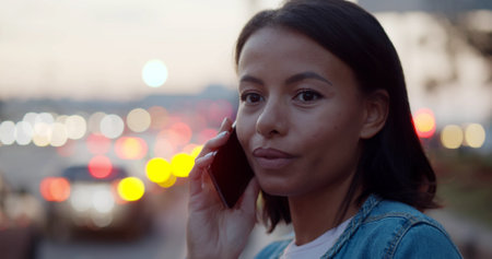 Bokeh shot of African-American-American woman having phone call in city evening with lights on backgroundの写真素材