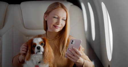 Beautiful rich woman with dog using smartphone in private first class planeの写真素材