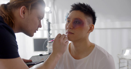 Male visagiste applying bruise makeup on face of young man before shooting sceneの写真素材