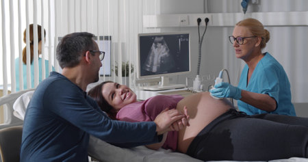 Happy couple making ultrasound of baby in clinic officeの写真素材