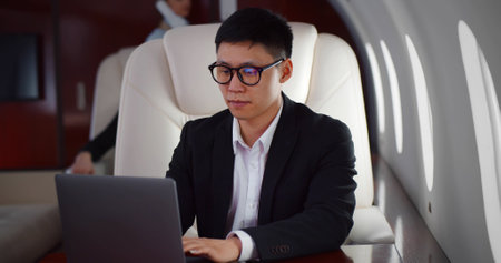Rich asian businessman flying first class and working on plane with laptopの写真素材