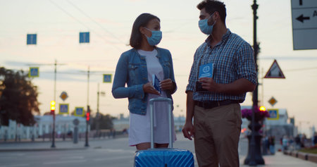 Multiethnic couple in safety mask standing outdoors with luggage and vaccine certificateの写真素材