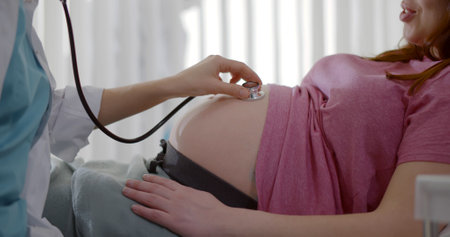 Gynecologist doctor hand checking pregnant young woman with stethoscopeの写真素材