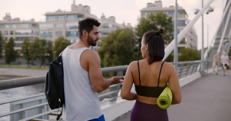 Follow shot of African-American woman and indian man runners walking in sportswear on city bridgeの写真素材