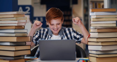Teen boy student feeling happy after accomplishing task sitting in libraryの写真素材
