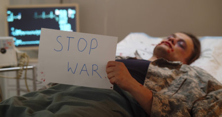 Wounded and weak soldier lying in hospital bed and holding stop war posterの写真素材