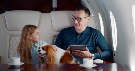 Mature businessman travelling on personal jet with little daughter and dogの写真素材