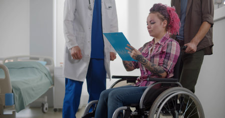 Young smiling woman patient in wheelchair signing discharge documents at hospital ward.の写真素材