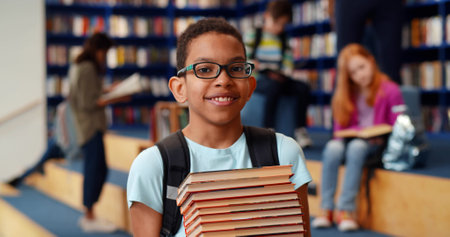 Middle eastern boy holding stack of books against multi colored bookshelf in library.の写真素材