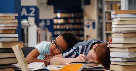 Diverse classmates falling asleep on desk with various book in libraryの写真素材