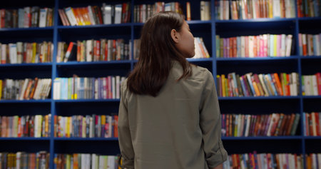 Back view of teen girl looking at bookshelves in library