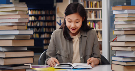 Asian school student girl reading book sitting at desk at libraryの写真素材