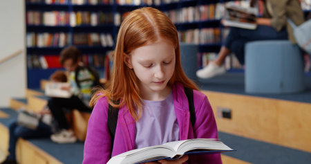 Redhead student girl reading book at school libraryの写真素材