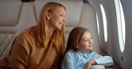 Mature elegant mother and preteen daughter looking through window flying on airplaneの写真素材