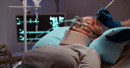 Injured woman with neck brace and oxygen mask in hospital bed, nurse treating forehead woundの写真素材