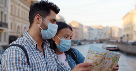 Couple with face mask looking at map exploring foreign city and traveling during pandemicの写真素材