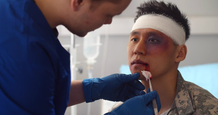 Close up of doctor cleaning wound on face of asian soldier in army hospitalの写真素材