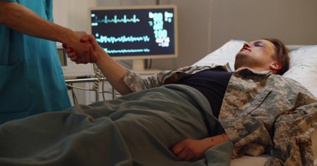 Injured soldier lying in hospital and shaking hands with doctorの写真素材