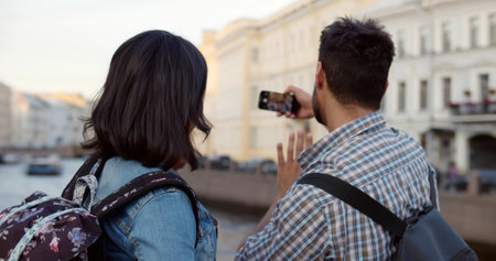 Back view of young couple on holidays taking selfie on cellphone in foreign cityの写真素材