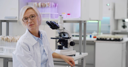 Mature female scientist using microscope studying samples in biotechnology labの写真素材