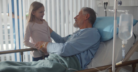 Little girl visiting ill grandfather in hospital room.の写真素材