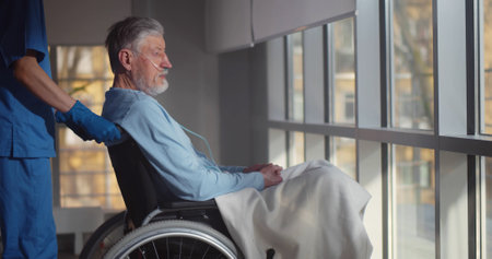 Nurse putting wheelchair with senior man with nasal oxygen tube near windowの写真素材