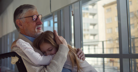 Preteen girl hugging grandfather in wheelchair visiting at hospitalの写真素材