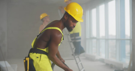 Shirtless African-American builder cleaning with construction vacuum cleaner