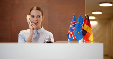 Smiling young businesswoman talking on telephone at receptionの写真素材