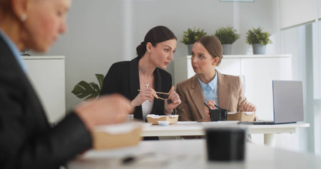 Business people sitting at table in front of laptop and having lunch together in officeの写真素材