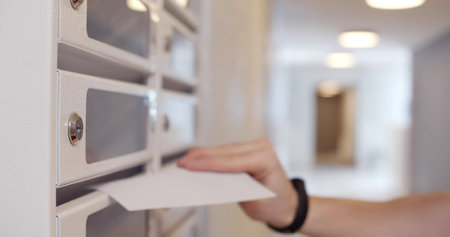Close up of postman putting letters in mailbox in apartment house lobby