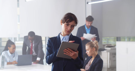 Confident young businesswoman using digital tablet with colleague at background in officeの写真素材