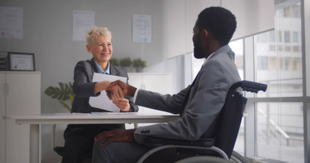 african-american disabled job candidate and mature female employer shaking hands and smiling at...