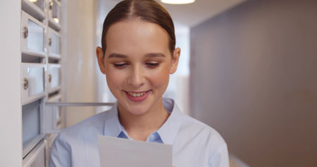 Happy woman reading received letter standing among mailboxes