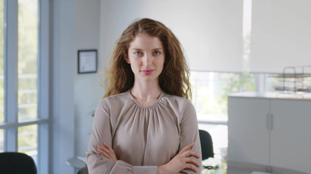 Confident young businesswoman with arms crossed standing in office looking at cameraの写真素材