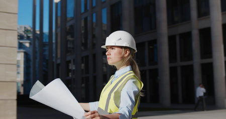 Architect in protective helmet holding blueprint in front of office buildingの写真素材