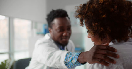 Caring African-American medical specialist comforting young woman patient in officeの写真素材